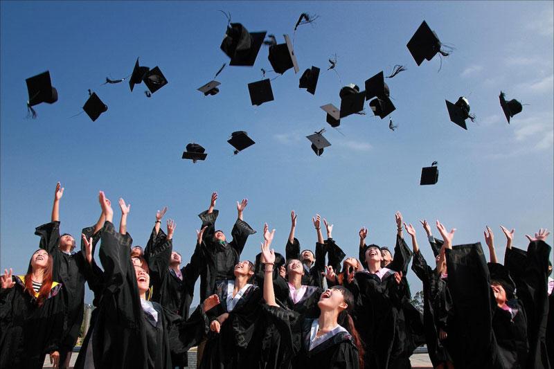 New graduates wearing gowns and throwing hats up in the air.
